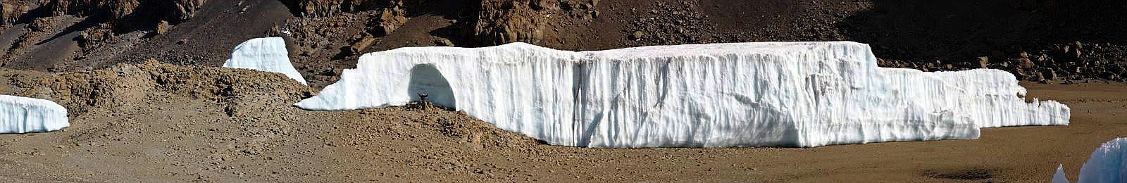 Das Südsegment des geteilten Furtwängler Gletscher in der Kibo-Kaldera im Jahr 2014 mit Eisgrotte und Person vor der Eisgrotte zum Größenvergleich